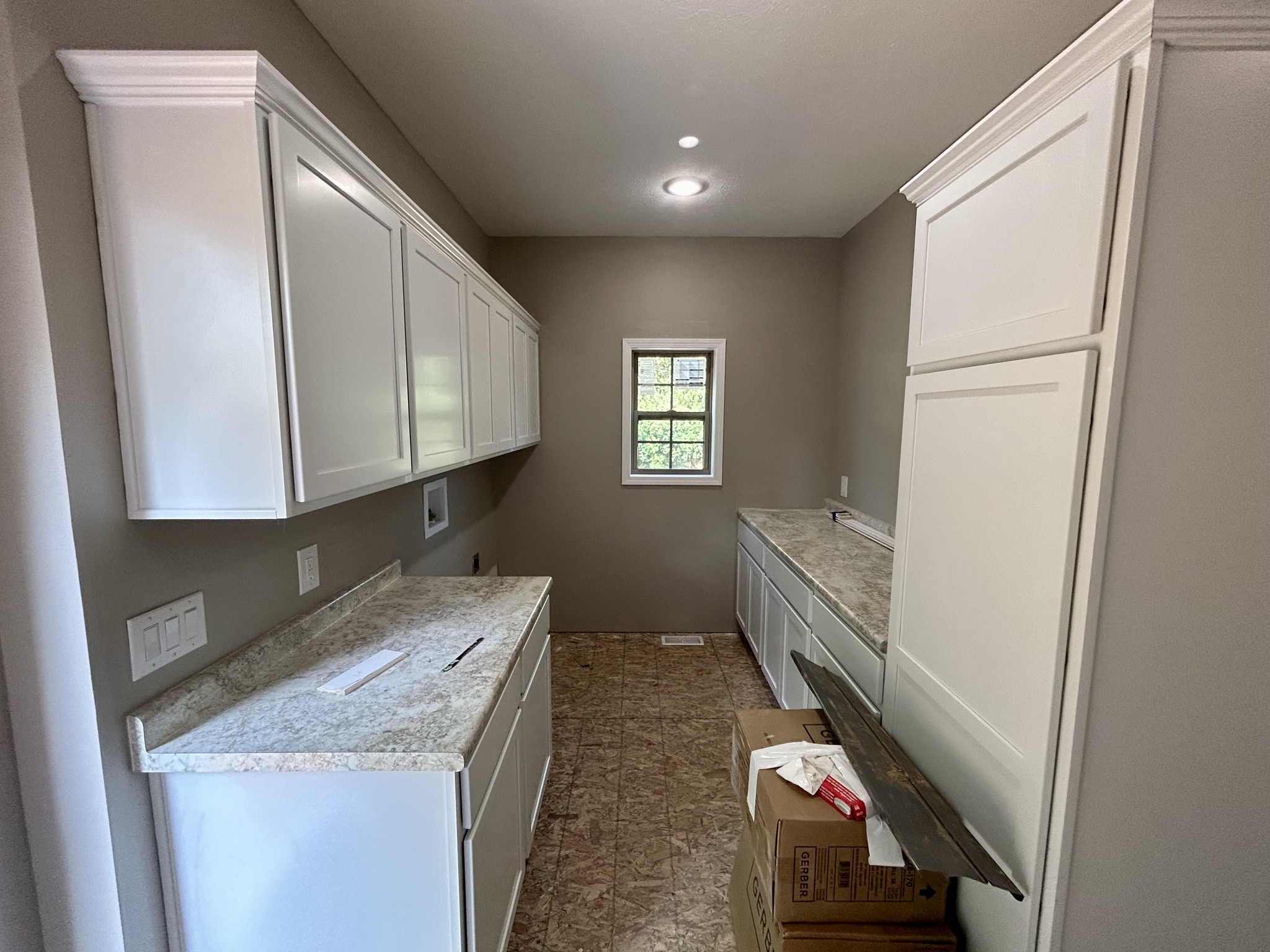 Newly renovated kitchen with white cabinets, marble countertops, and a small window. Cardboard boxes and a wood plank on the floor suggest ongoing work.