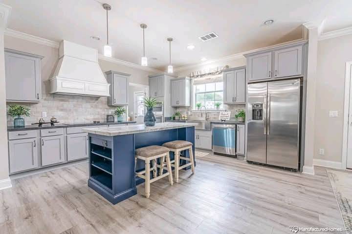 Modern kitchen with gray cabinets, stainless steel appliances, and a central island with blue base. Two stools and plants create a welcoming vibe.
