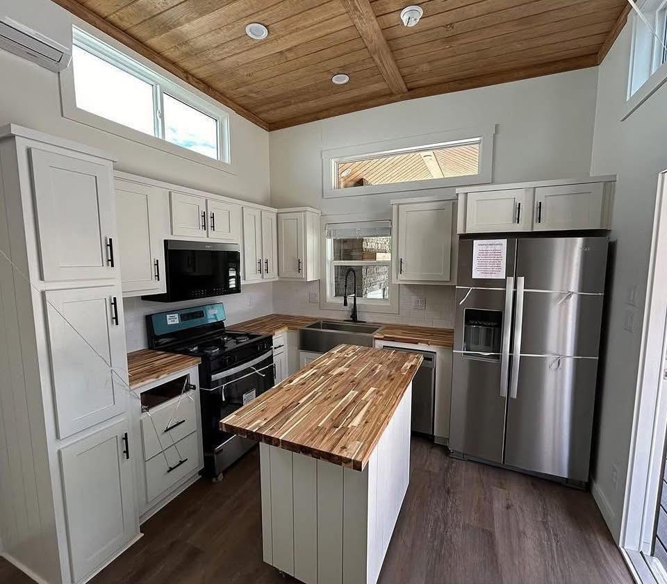 Modern kitchen with wooden ceiling, white cabinets, stainless steel appliances, butcher block countertops, and a central island. Bright and cozy atmosphere.