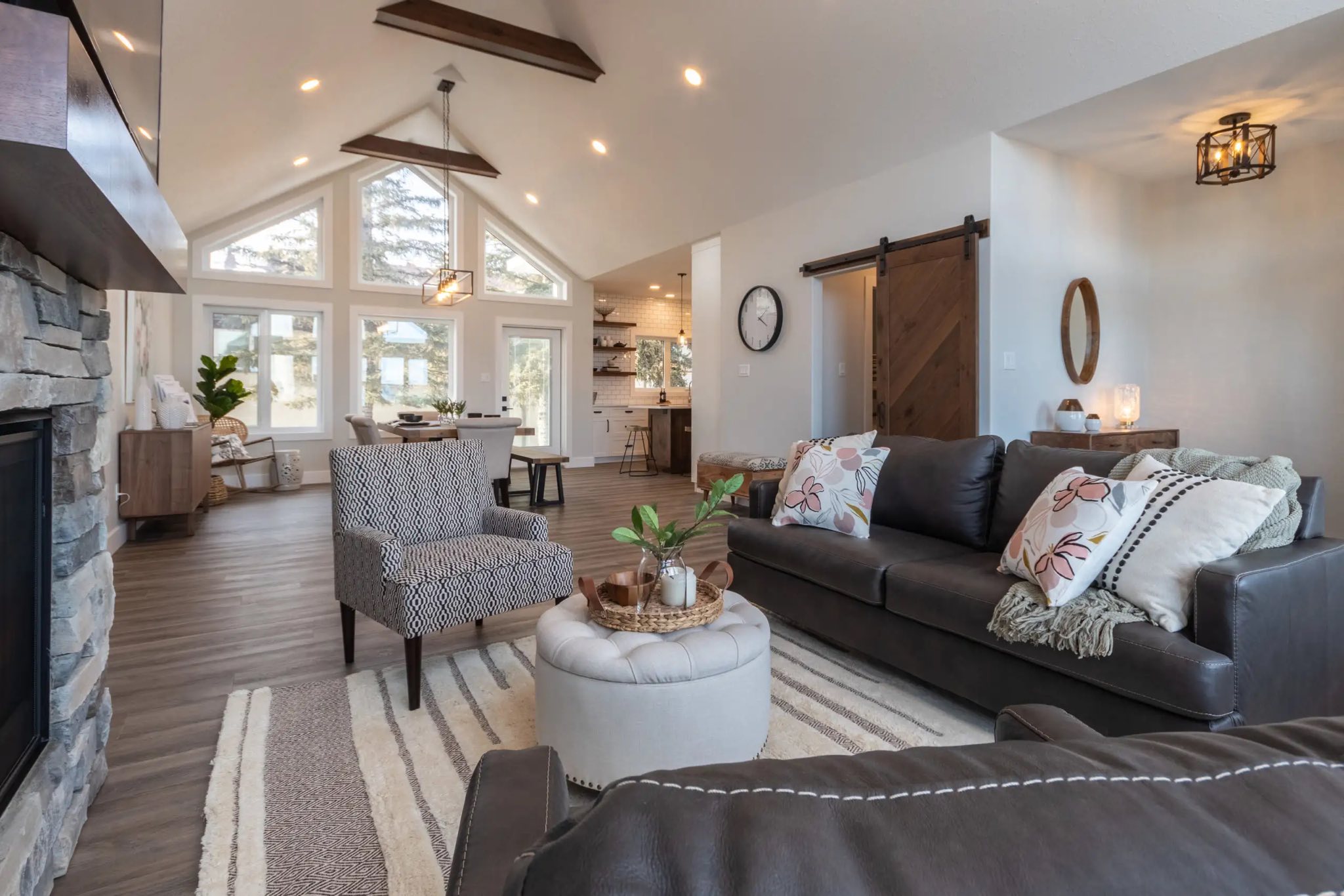 Spacious, inviting living room with high ceilings and large windows. Features cozy sofas, patterned armchair, warm tones, and modern decor.