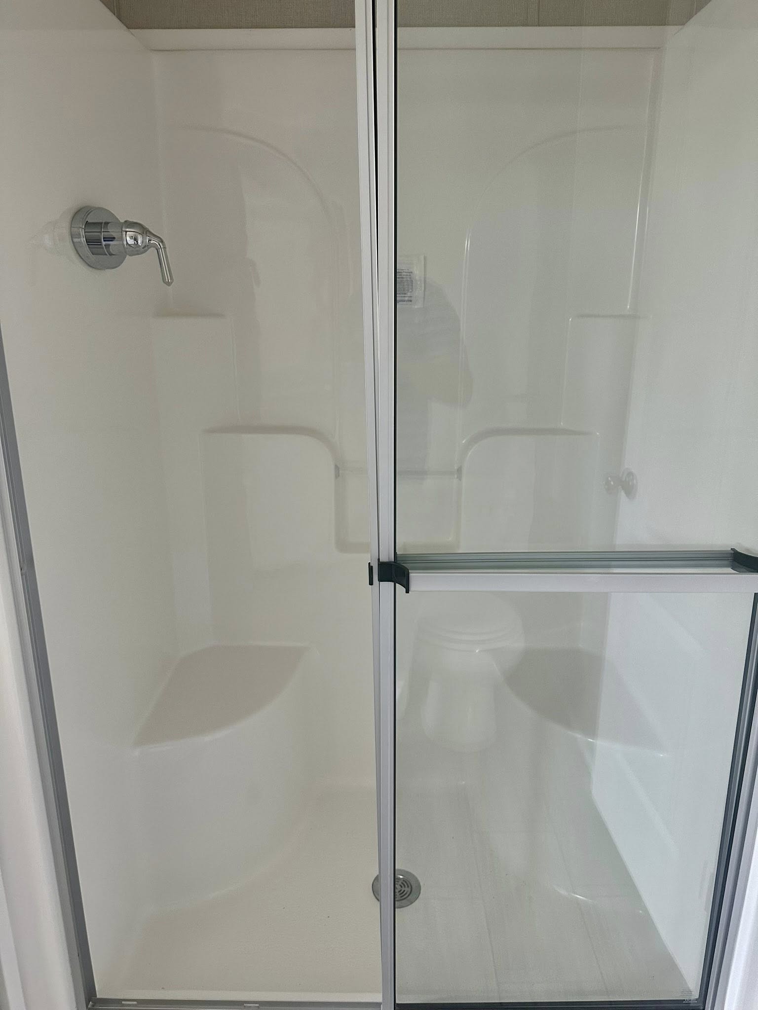 Modern bathroom shower with glass doors, featuring a chrome faucet, built-in white seating and shelves. Clean, minimalist design.