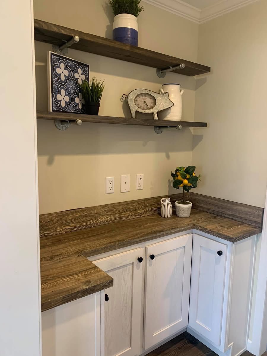 Cozy corner with rustic wood shelves holding plants, decor, and a clock. White and wood cabinets below, with a small citrus plant on the counter.