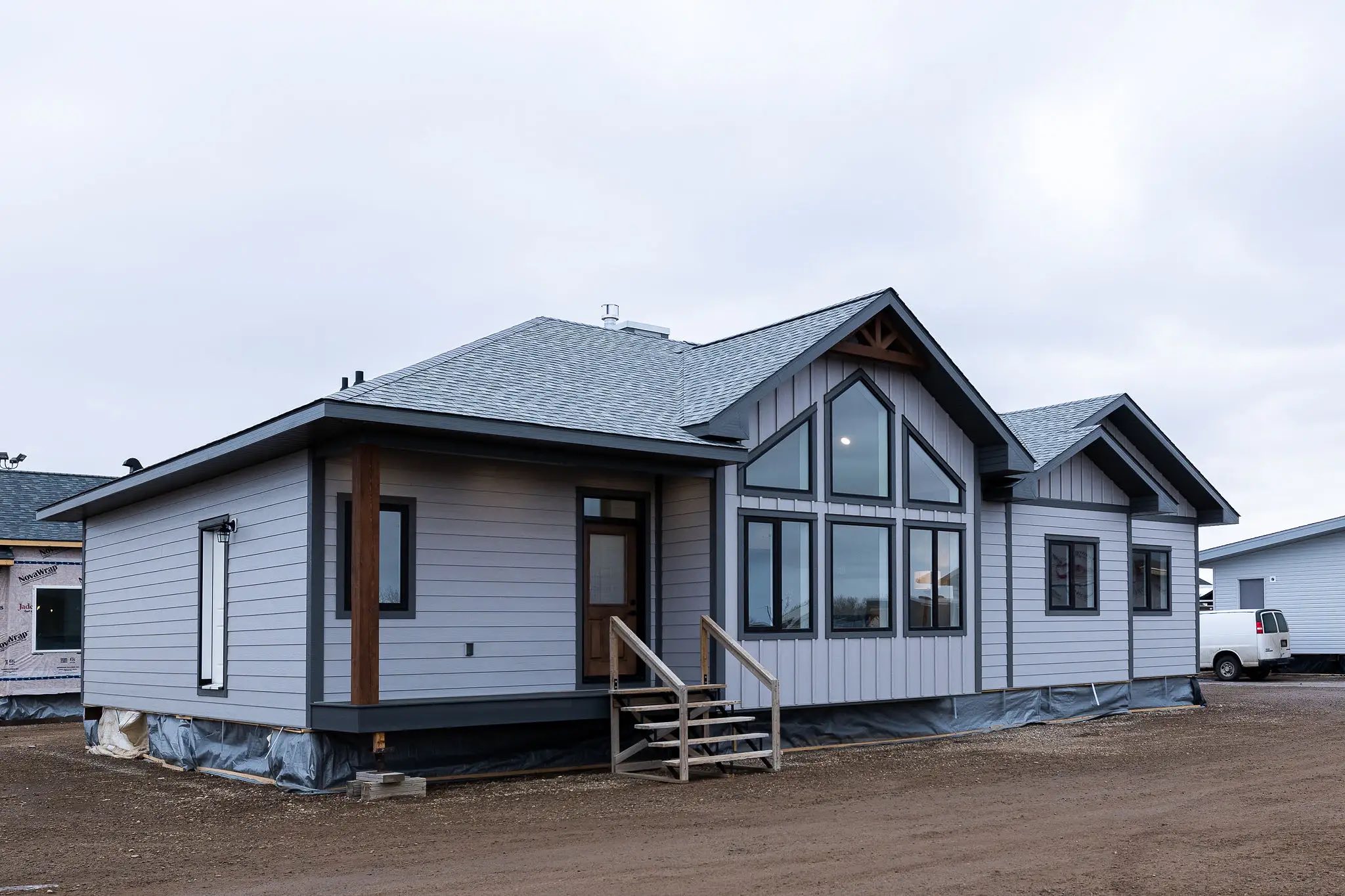 Modern, single-story house with gray and white paneling, large windows, and a sloped roof. Set on a cloudy day, the scene feels serene and spacious.