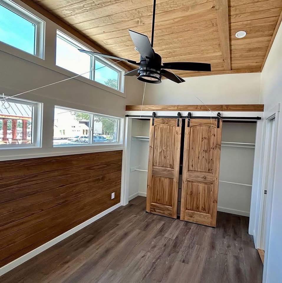 Room with wood plank accents, double sliding barn doors, and a ceiling fan. The large windows illuminate the space, creating a warm, rustic feel.