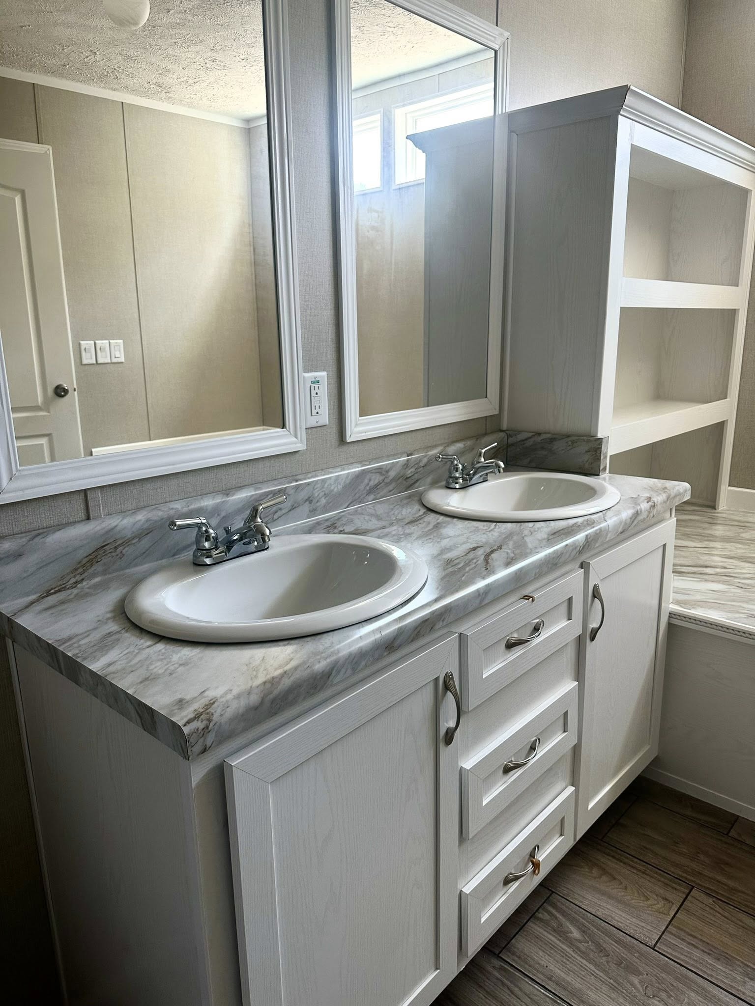 Modern bathroom with two white sinks on a marble countertop, a large mirror, and wooden cabinets. The tone is clean and minimalist.
