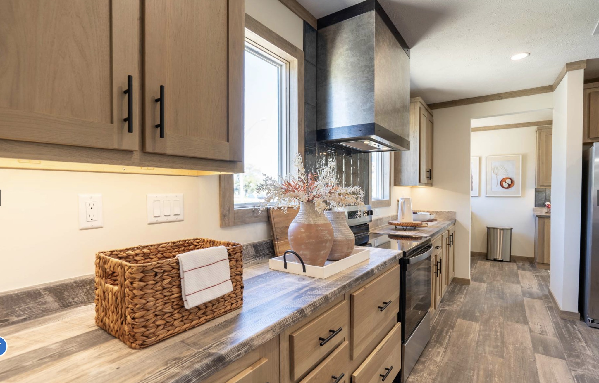 Modern kitchen with wooden cabinets and a sleek countertop. A woven basket and decorative vase sit under a window, creating a cozy ambiance.