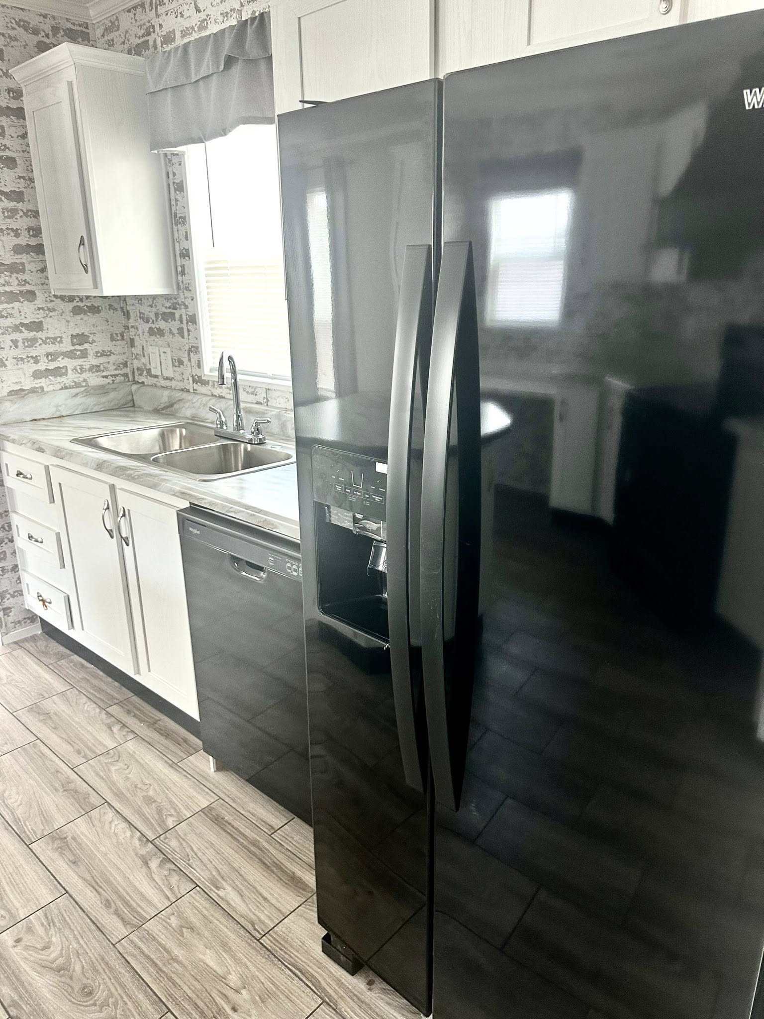 Modern kitchen with a sleek black fridge, adjacent to a stainless steel sink and white cabinets. Brick-patterned backsplash adds a chic touch.