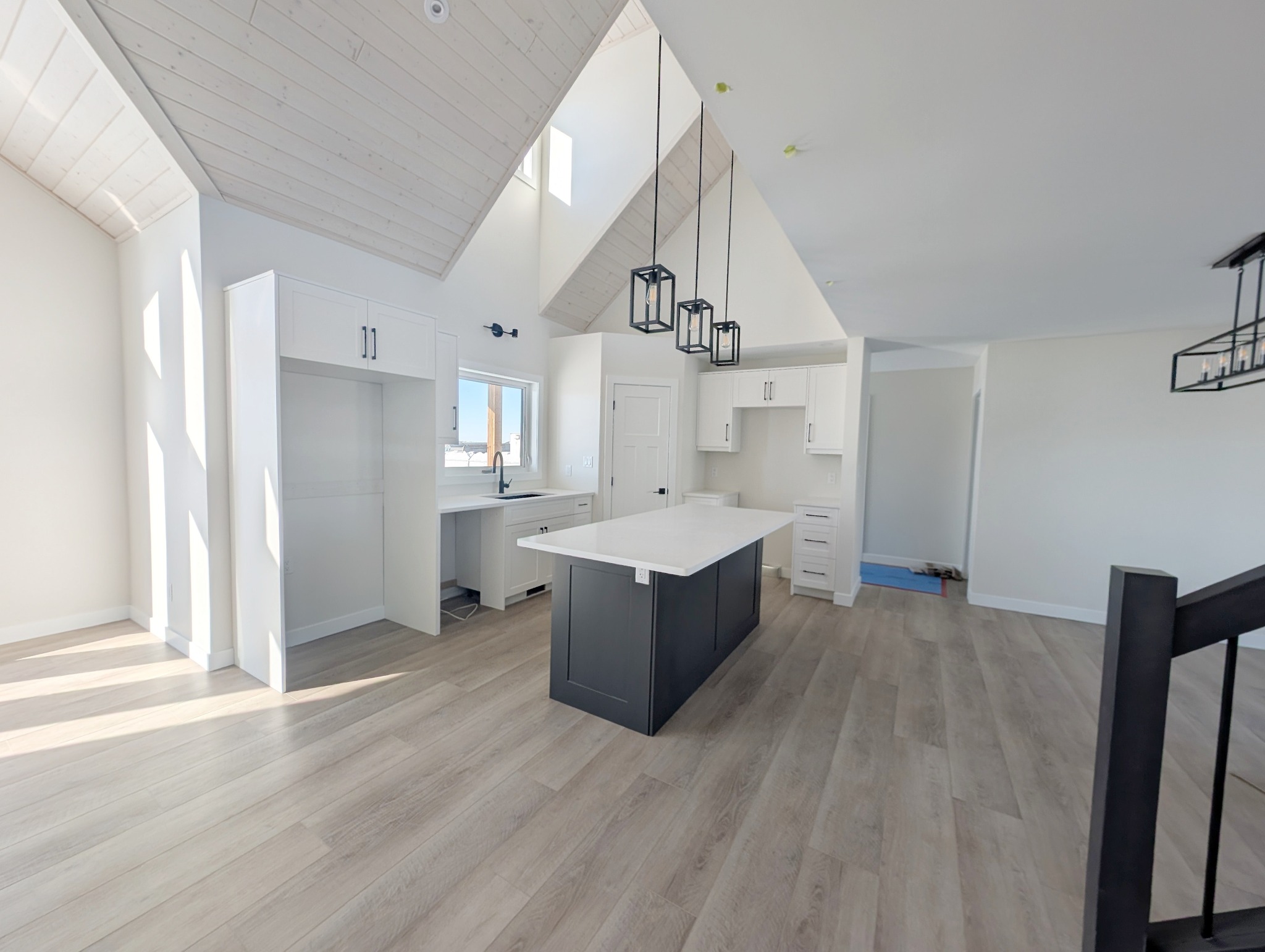 Spacious, modern kitchen with white cabinets, a large black island, and light wood flooring. High ceiling and large windows create an airy feel.