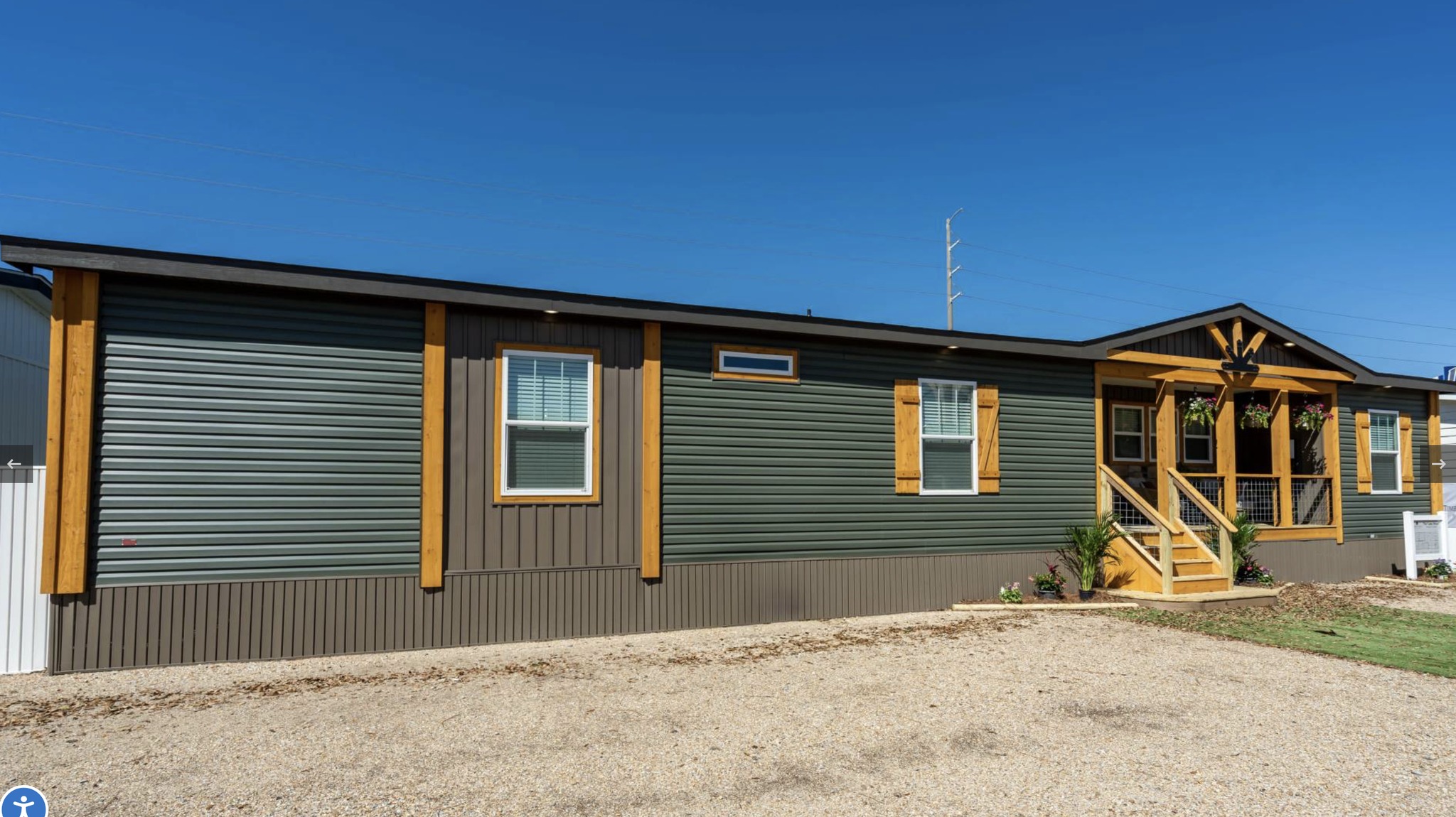 Modern modular home with green siding and wooden accents, featuring a welcoming porch and steps. Clear blue sky enhances the bright, inviting tone.