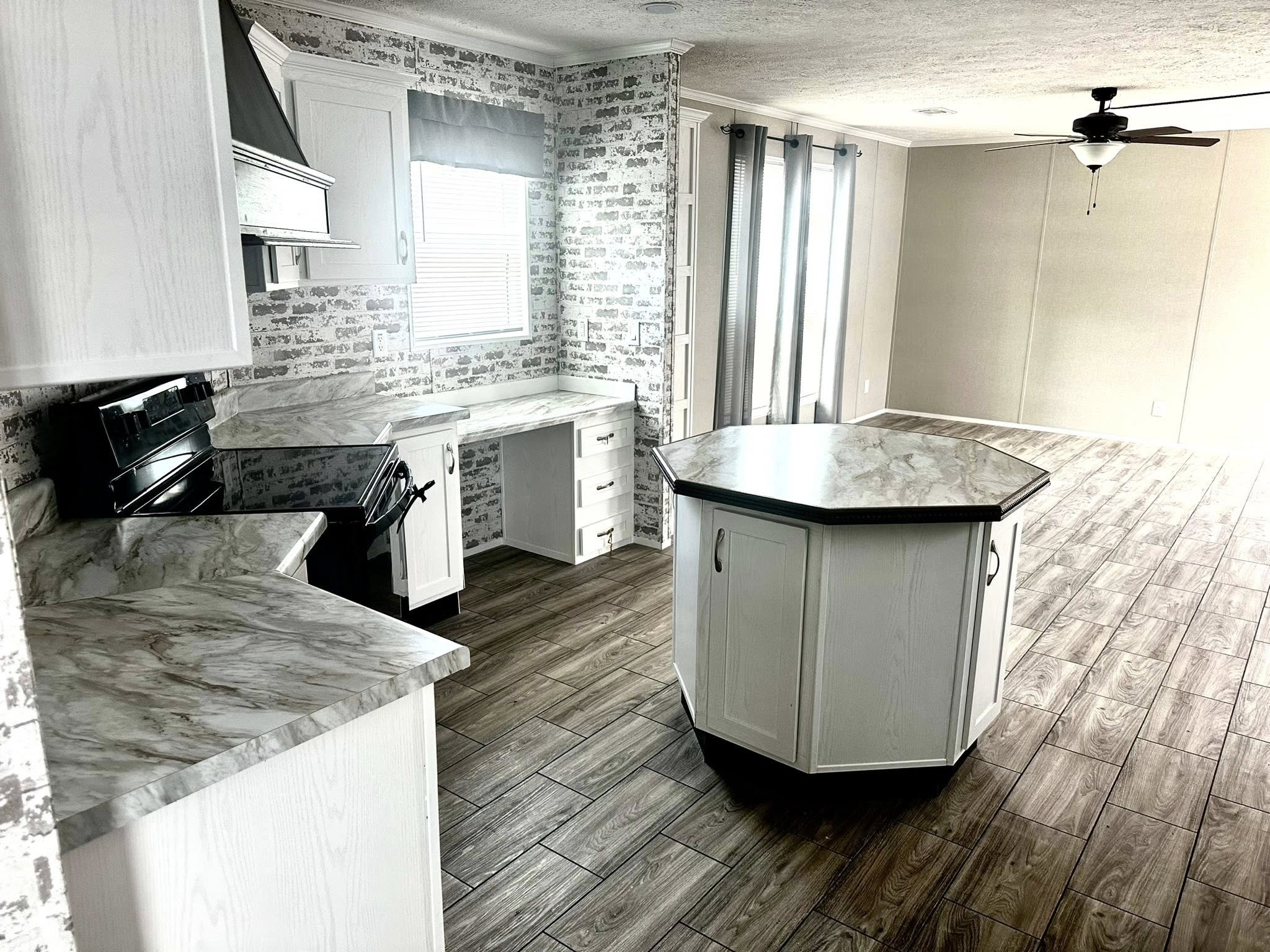 Spacious kitchen with marble countertops, white cabinets, and a central island. Brick-patterned walls, wood flooring, and ceiling fan create a modern feel.