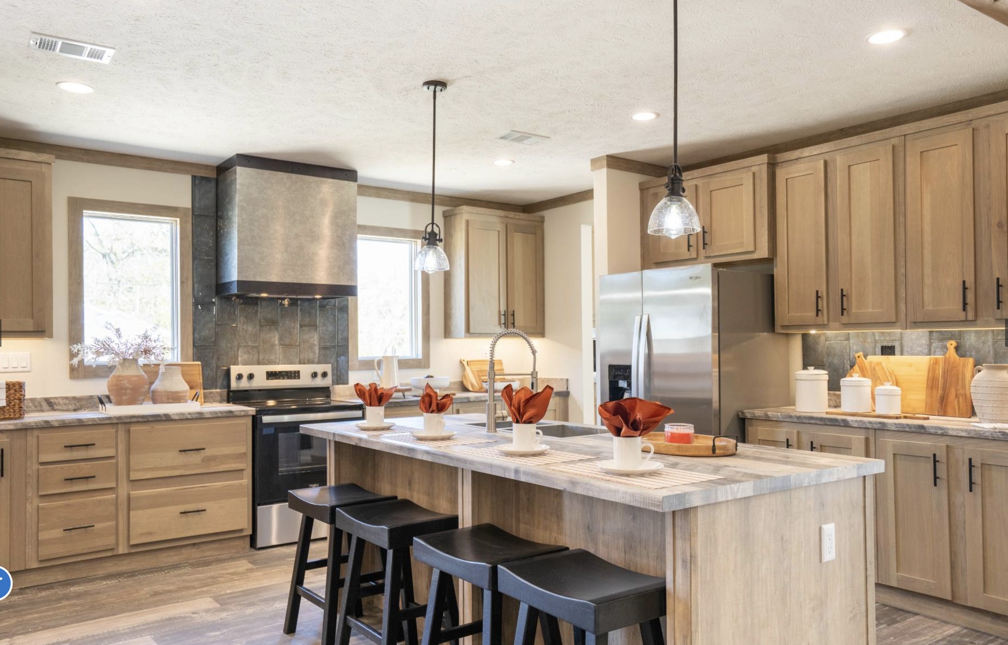 Modern kitchen with wooden cabinets, stainless steel appliances, and an island with stools. Warm lighting and decorative vases create a cozy atmosphere.