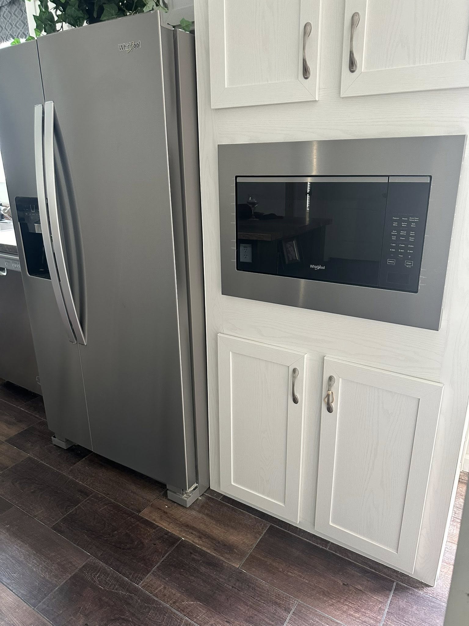 Modern kitchen with a stainless steel refrigerator and built-in microwave. White cabinets provide a clean look. The atmosphere is sleek and tidy.