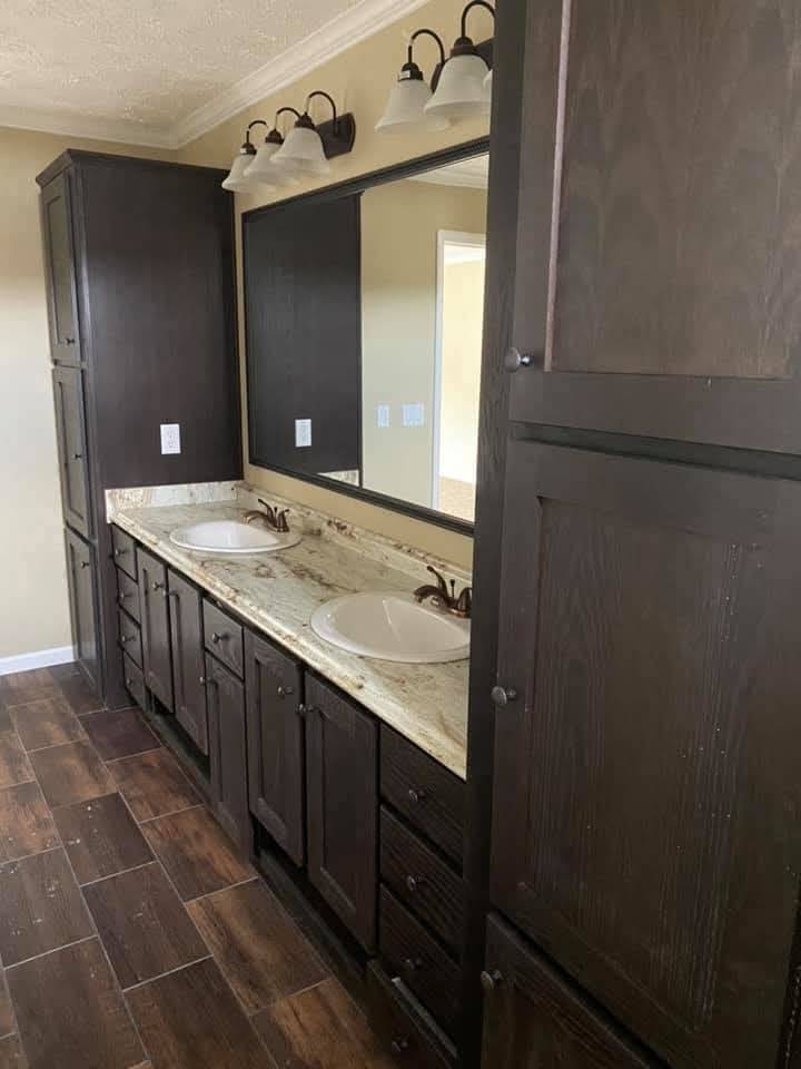 Spacious bathroom with dark wood cabinets and dual sinks on a speckled countertop. Large mirror with overhead lighting adds an elegant touch.