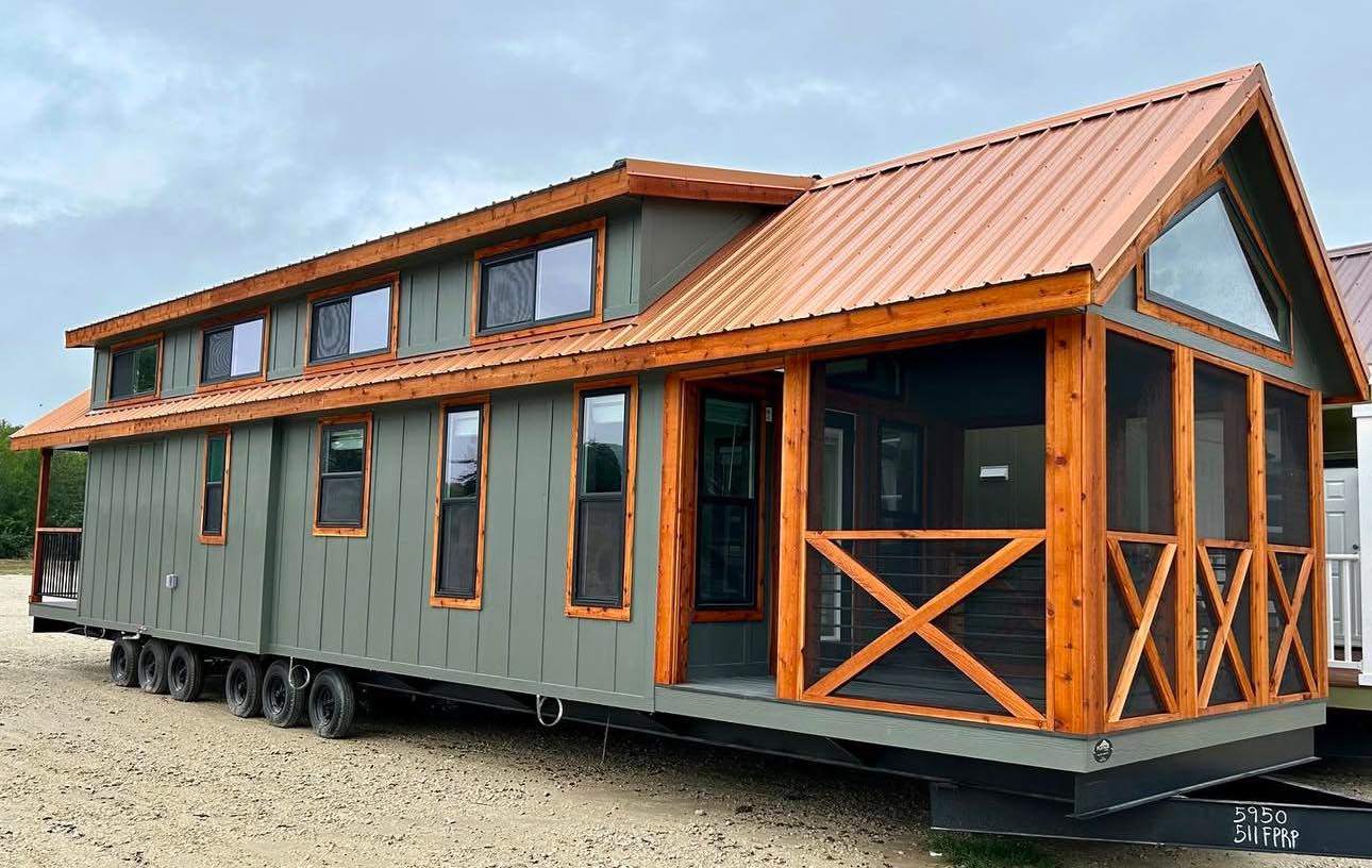 A modern tiny house on wheels with a green exterior and contrasting wooden trim. It features angular roofs and a screened porch, creating a cozy, inviting vibe.