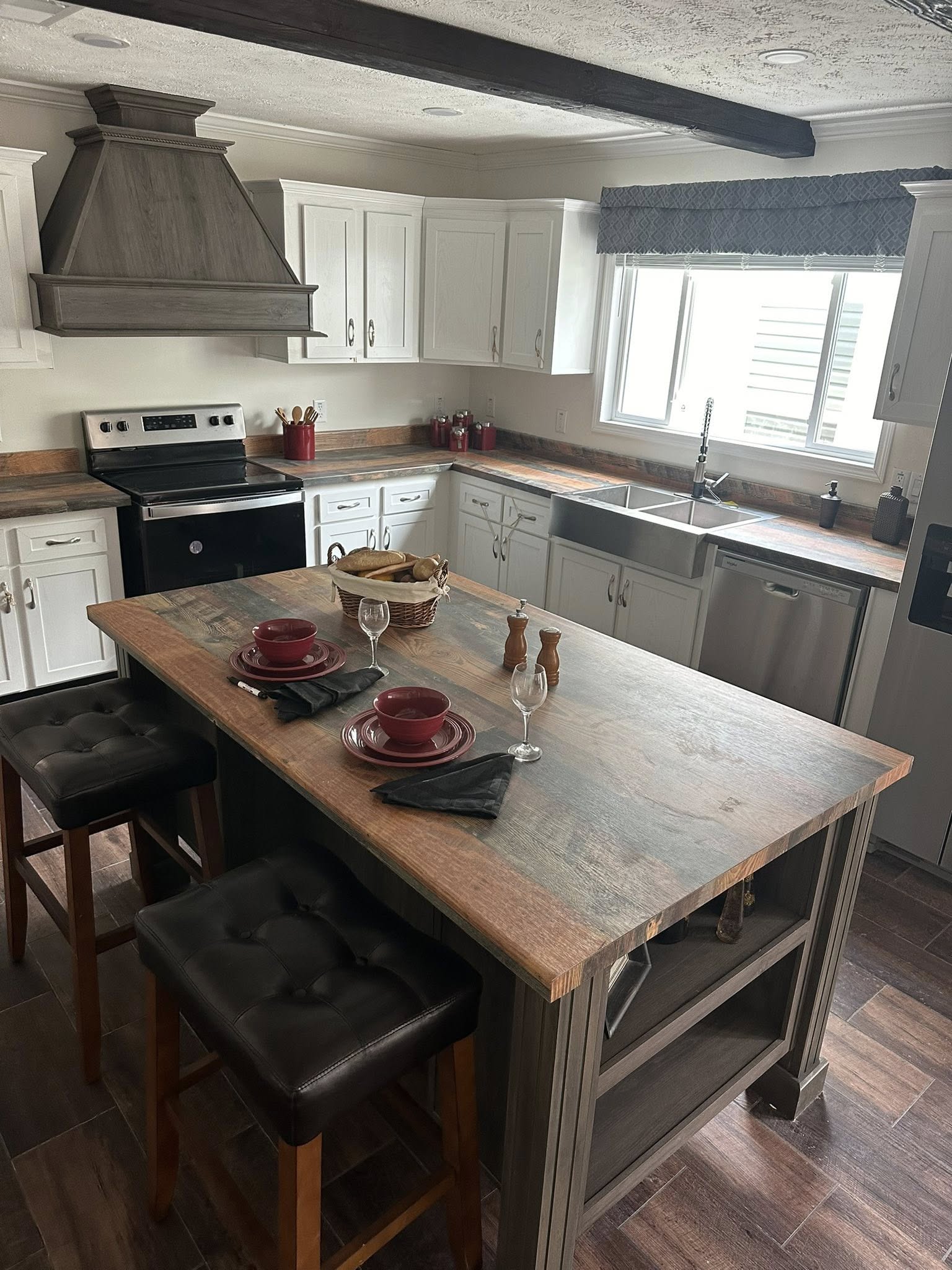 Rustic kitchen with gray cabinets and wood countertops. A central island set for two with red plates, black napkins, and wine glasses. Cozy ambiance.