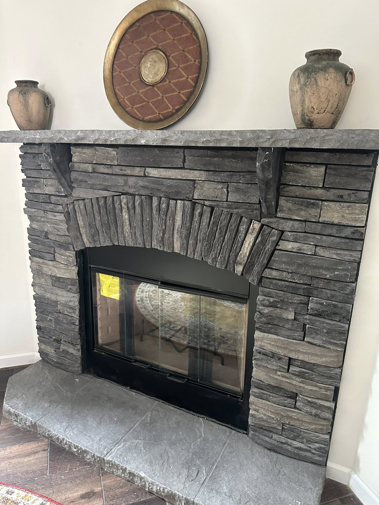 Stone fireplace with a rustic mantel, featuring two ceramic vases and a circular red and gold decorative plate. Warm, earthy tones create a cozy ambiance.