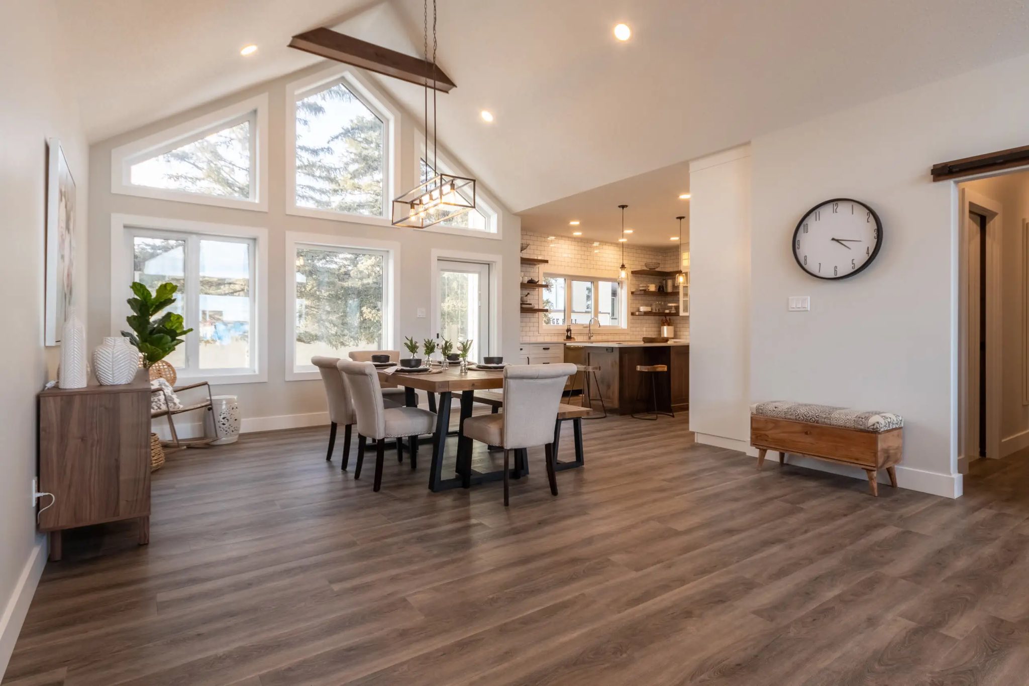 Spacious dining area with large windows and a vaulted ceiling. Modern decor, wooden floors, and soft lighting create a warm, inviting atmosphere.