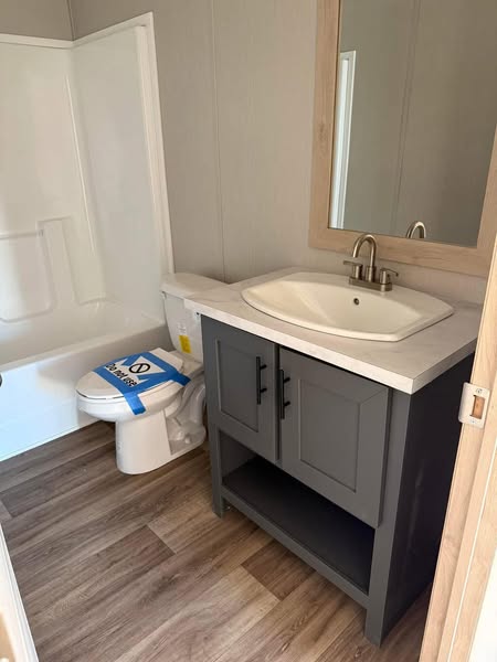 Modern bathroom with gray vanity, white sink, and mirror. A toilet with a "Do Not Use" sign is next to a white bathtub. The space is well-lit with a clean, minimalist design.