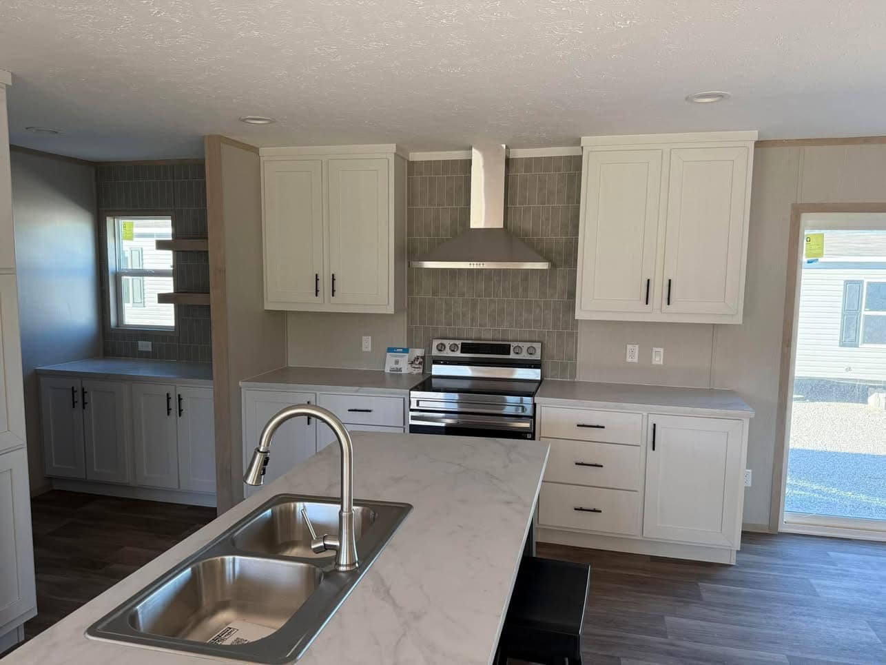 Modern kitchen with light cabinets, stainless steel stove and hood, tiled backsplash, and a marble island with sink. Bright and minimalistic.