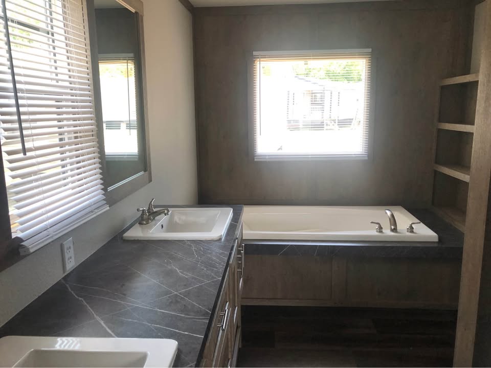Modern bathroom with dark marble countertops featuring dual sinks and chrome faucets. A sunlit bathtub is centered under a window, enhancing a cozy ambiance.