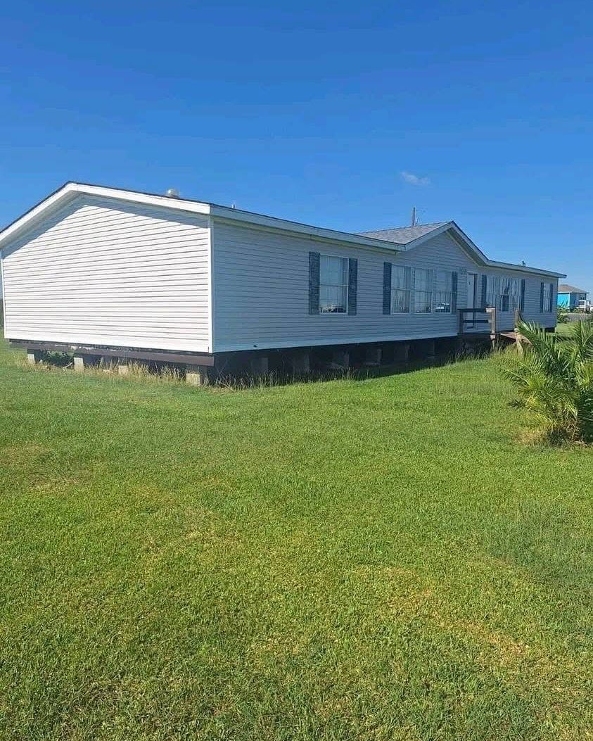A white single-story manufactured home with large windows sits on a lush green lawn under a clear blue sky, conveying a peaceful suburban setting.