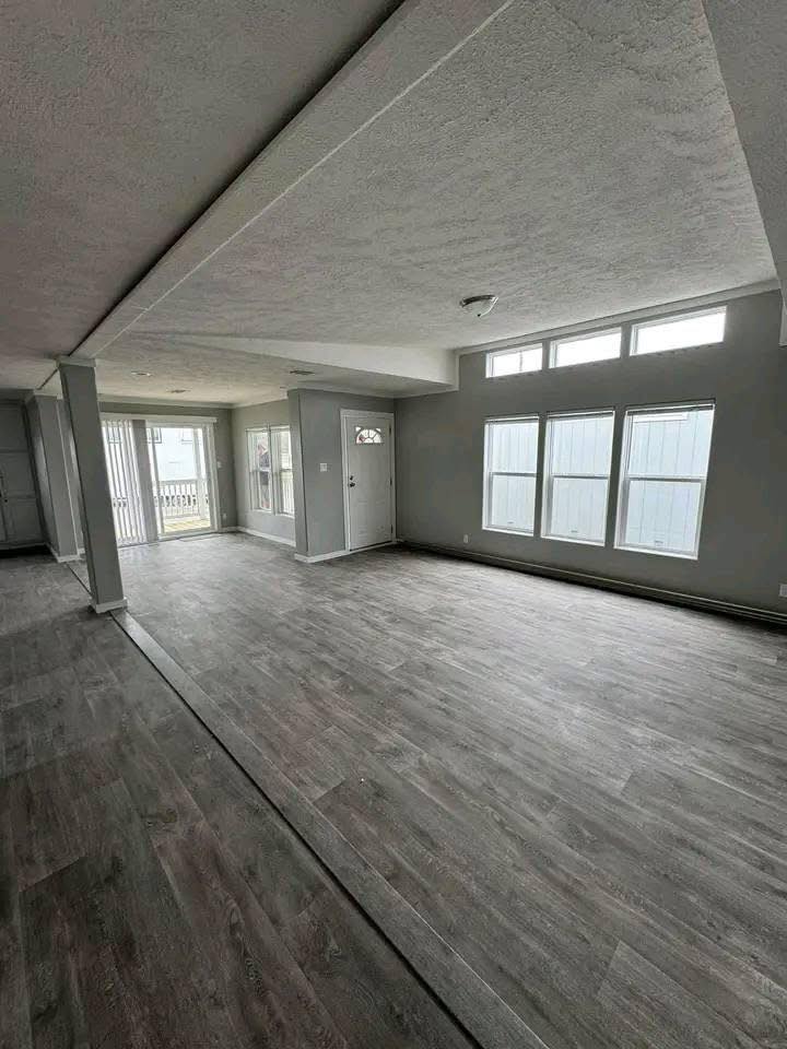 Spacious, empty living room with gray walls and large windows. Light wood flooring, natural light, minimalistic and inviting atmosphere.