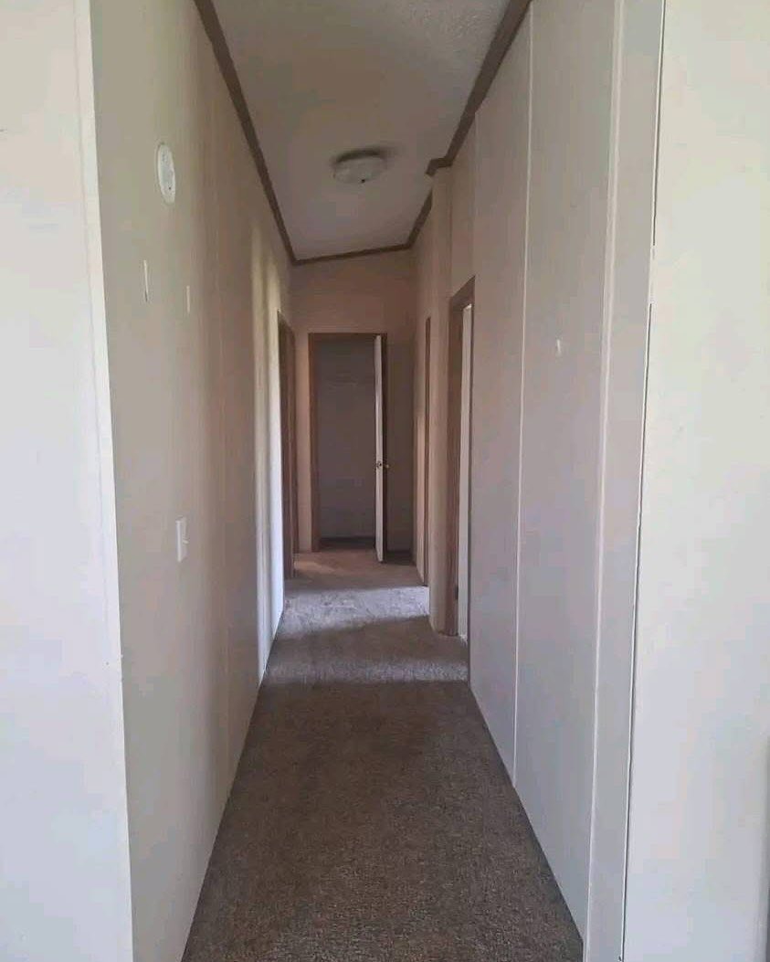 Narrow, carpeted hallway with beige walls and a ceiling light. Two doors are visible on the left side and one at the end, slightly ajar, creating a calm, empty tone.
