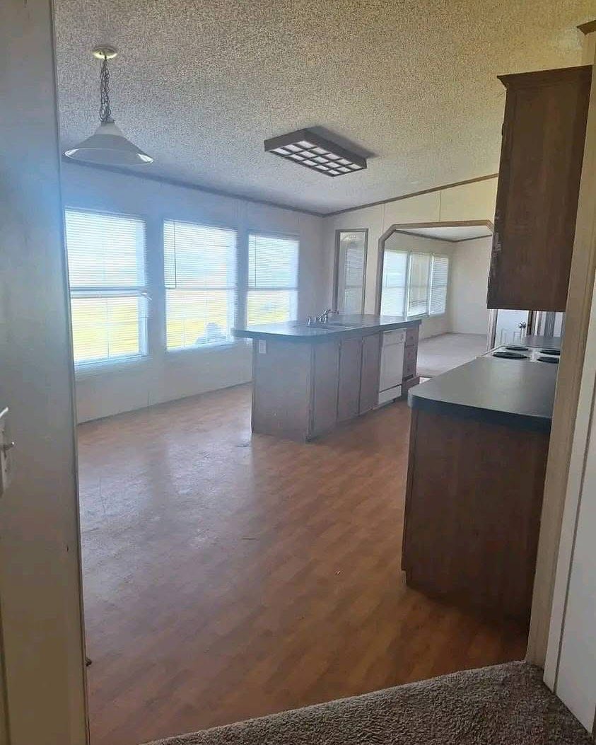 Bright kitchen with wooden floors, featuring a central island and modern appliances. Large windows fill the room with natural light, creating an inviting atmosphere.