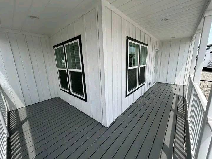 White-paneled porch with gray wooden floorboards and two corner windows with black trim. Bright and clean ambiance with shadows cast by railings.