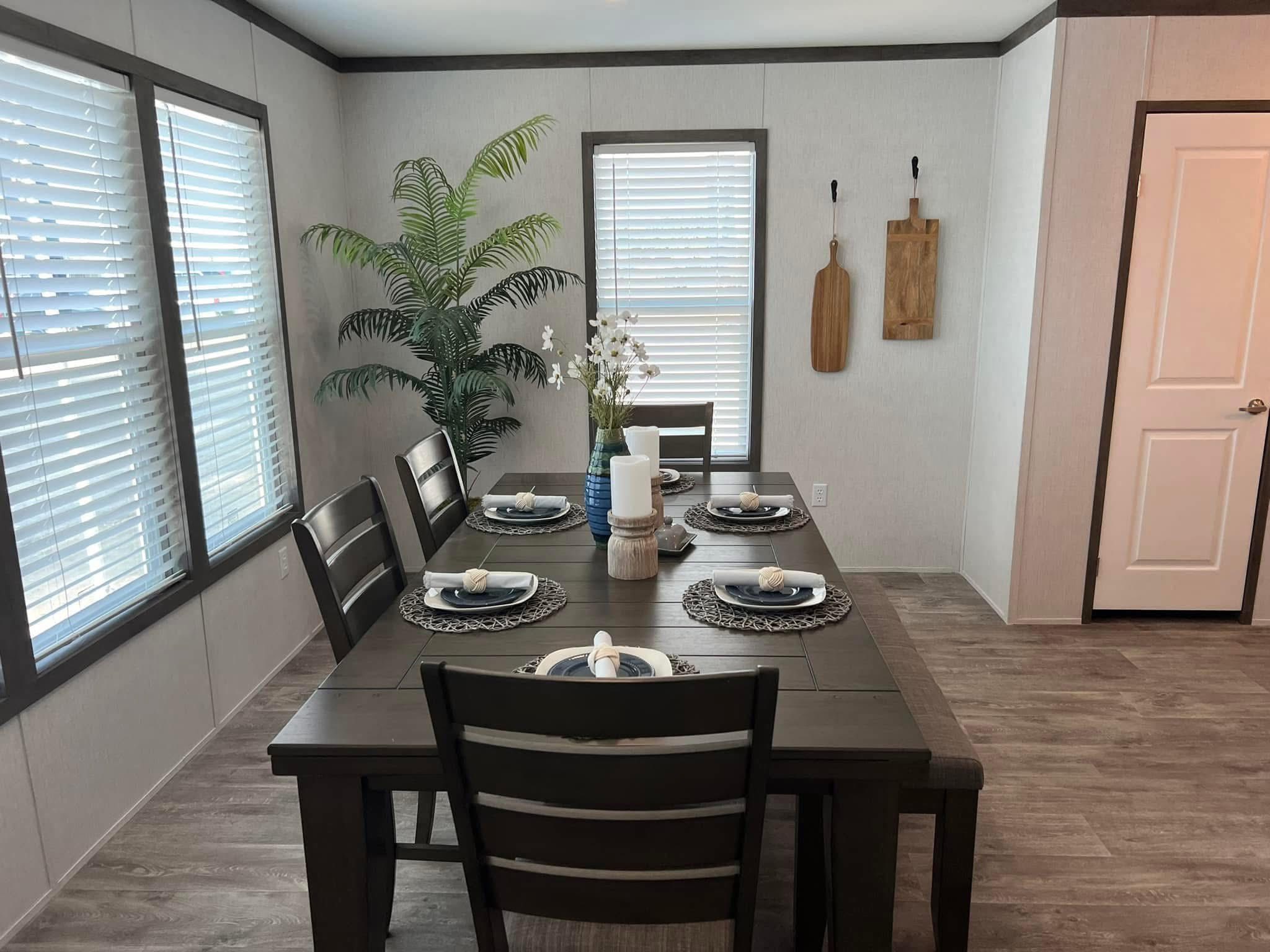 Modern dining room with a dark wood table set for six, featuring black plates and white napkins. A large potted plant and wall decor add elegance.