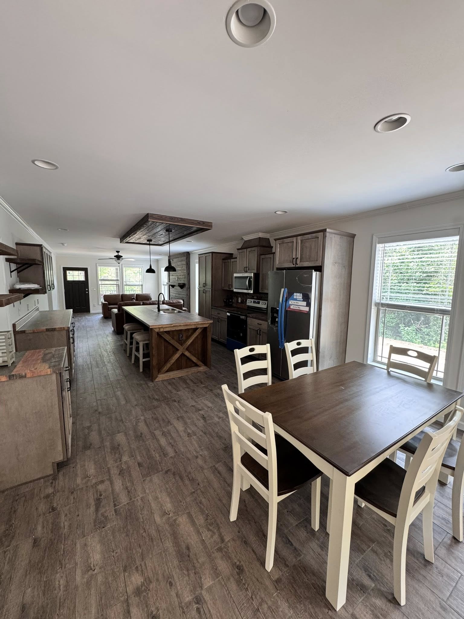 Spacious kitchen with wooden floors, central island, and dining table. Modern stainless steel appliances and large windows create a cozy, inviting atmosphere.