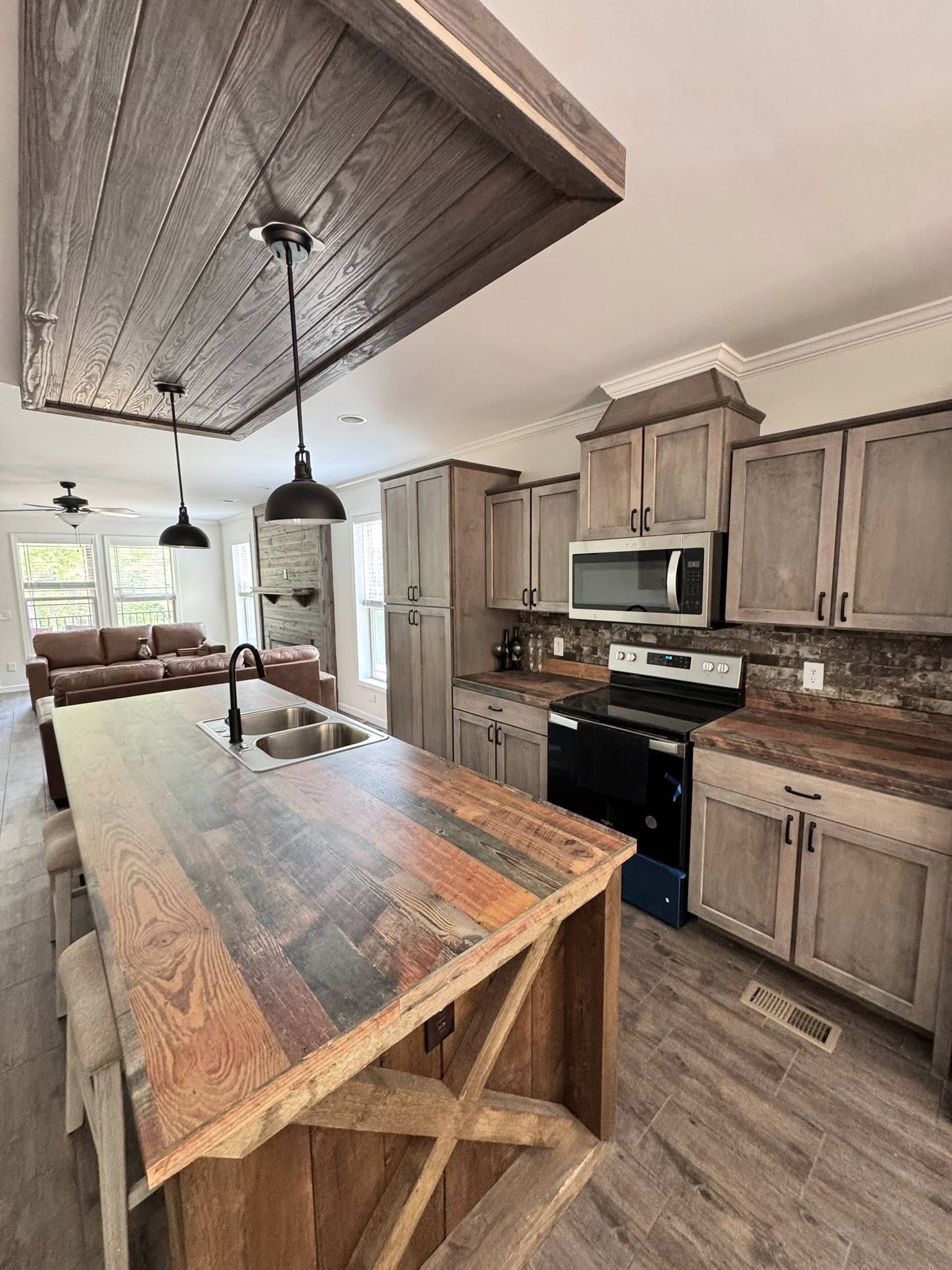 Stylish kitchen with rustic wood cabinetry and countertops, modern appliances, and two pendant lights above an island. Connected living area visible.