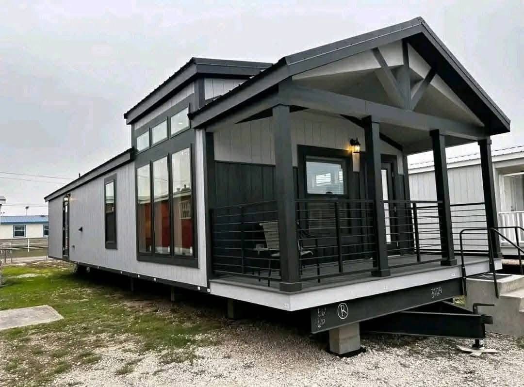 Modern mobile home with a dark and light gray exterior, large windows, and a small covered porch. The atmosphere is calm and welcoming.