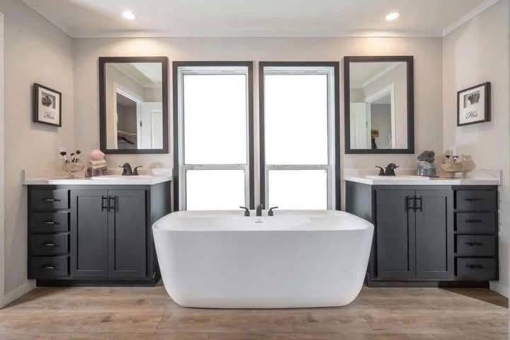 Modern bathroom with a central white freestanding tub, flanked by two sinks with dark cabinets and mirrors. Soft lighting creates a serene atmosphere.