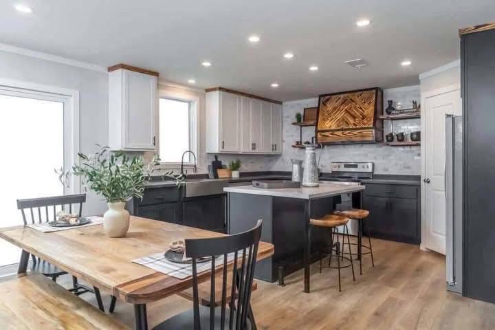 Modern kitchen with a warm, inviting atmosphere. Features white and dark cabinets, a central island with wooden stools, and a wooden dining table set.
