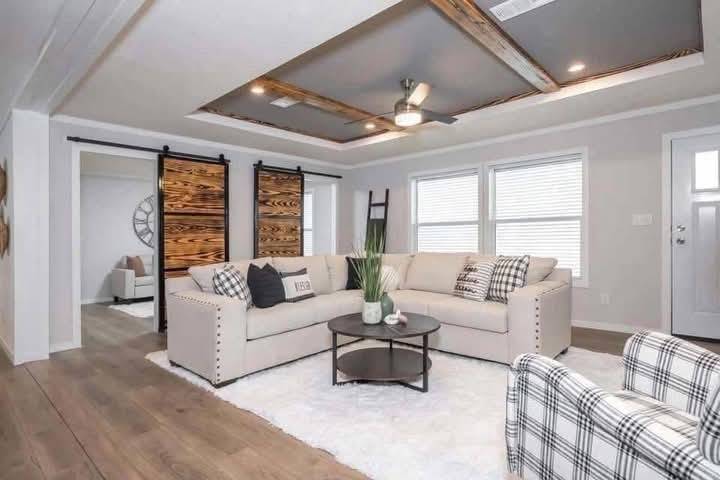 Stylish living room with L-shaped beige sofa, plaid chair, and round coffee table on a white rug. Highlights include wood accent ceiling and sliding barn doors.
