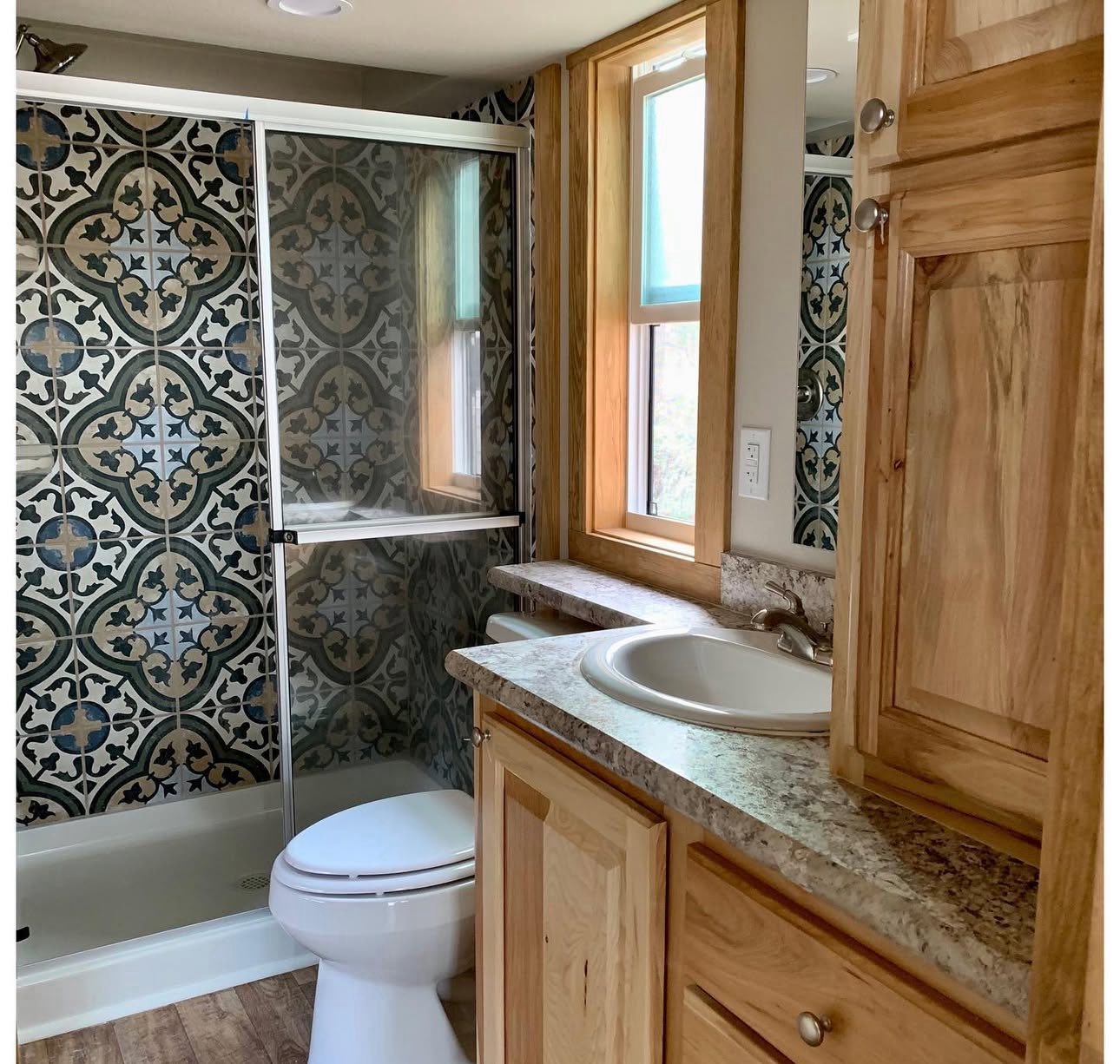 Compact bathroom featuring patterned tile walls, a glass shower door, wood accents, and a granite countertop with a sink, creating a cozy feel.