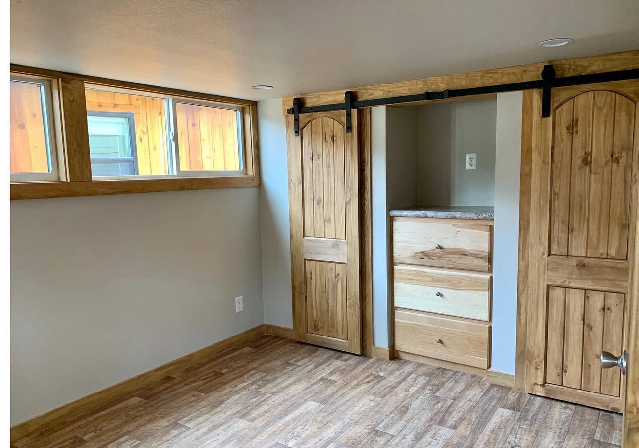 Cozy room with light wood floors, light walls, and two wooden sliding barn doors. Natural light pours in from tall windows, creating a warm atmosphere.