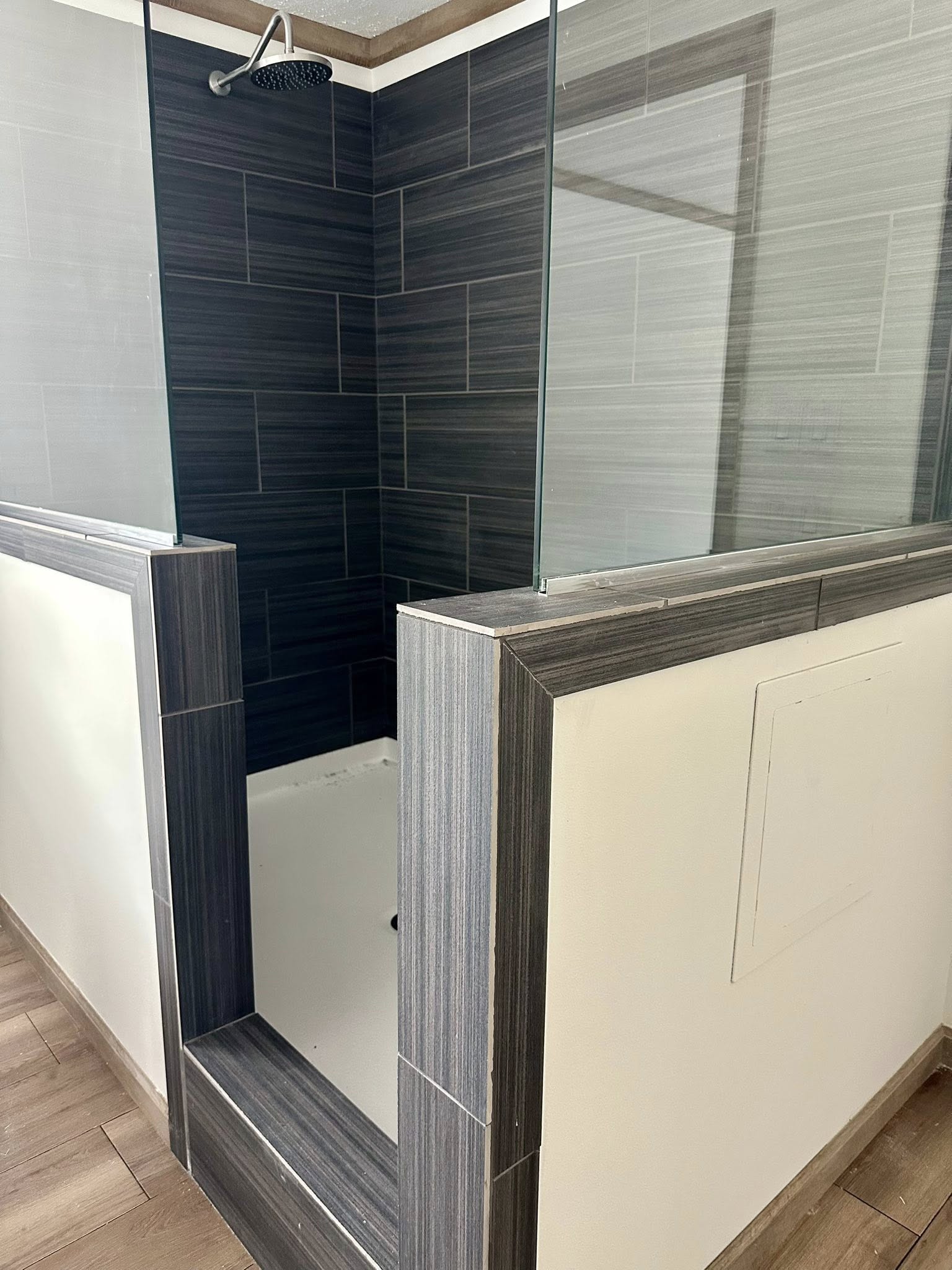 Modern shower with dark gray tiles and glass walls, featuring a rainfall showerhead. The space is clean and minimalist, conveying a sleek, contemporary feel.