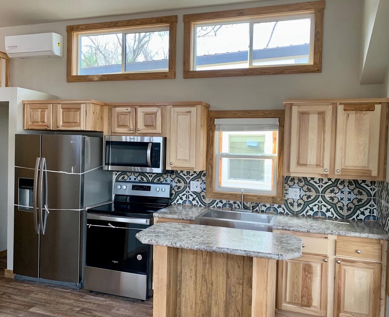 Modern kitchen with light wood cabinets, stainless steel appliances, and decorative tile backsplash. Granite countertops, bright windows, and wood accents enhance the cozy atmosphere.