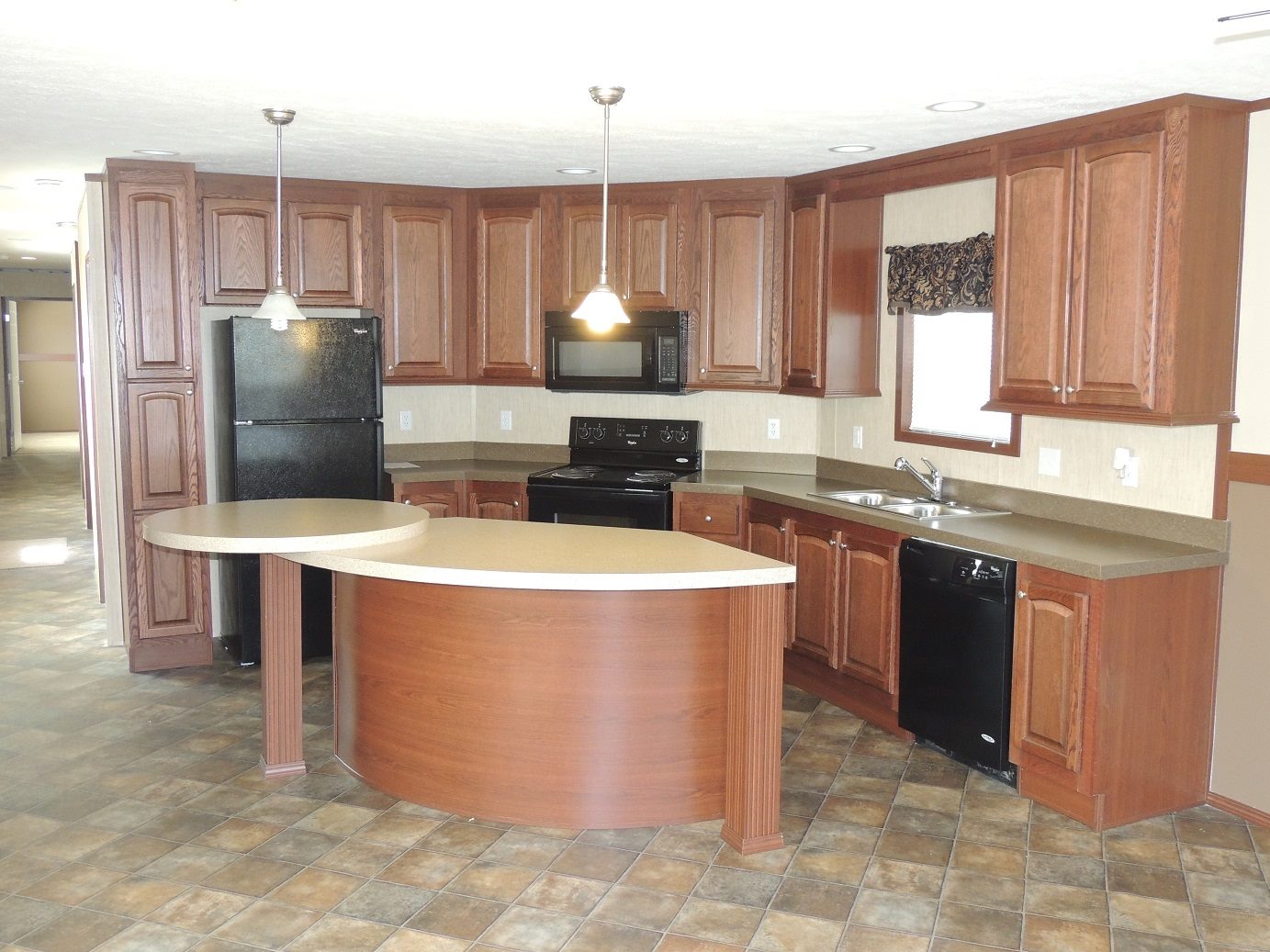 Spacious kitchen with curved island, dark wood cabinets, black appliances, and tiled floor. Pendant lights add warmth to the modern design.