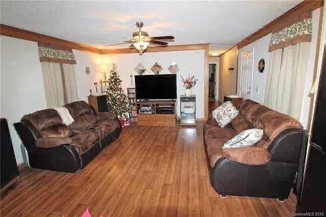 Living room with brown sofas facing a TV on a wooden floor. A decorated Christmas tree and wall decorations create a cozy, festive atmosphere.