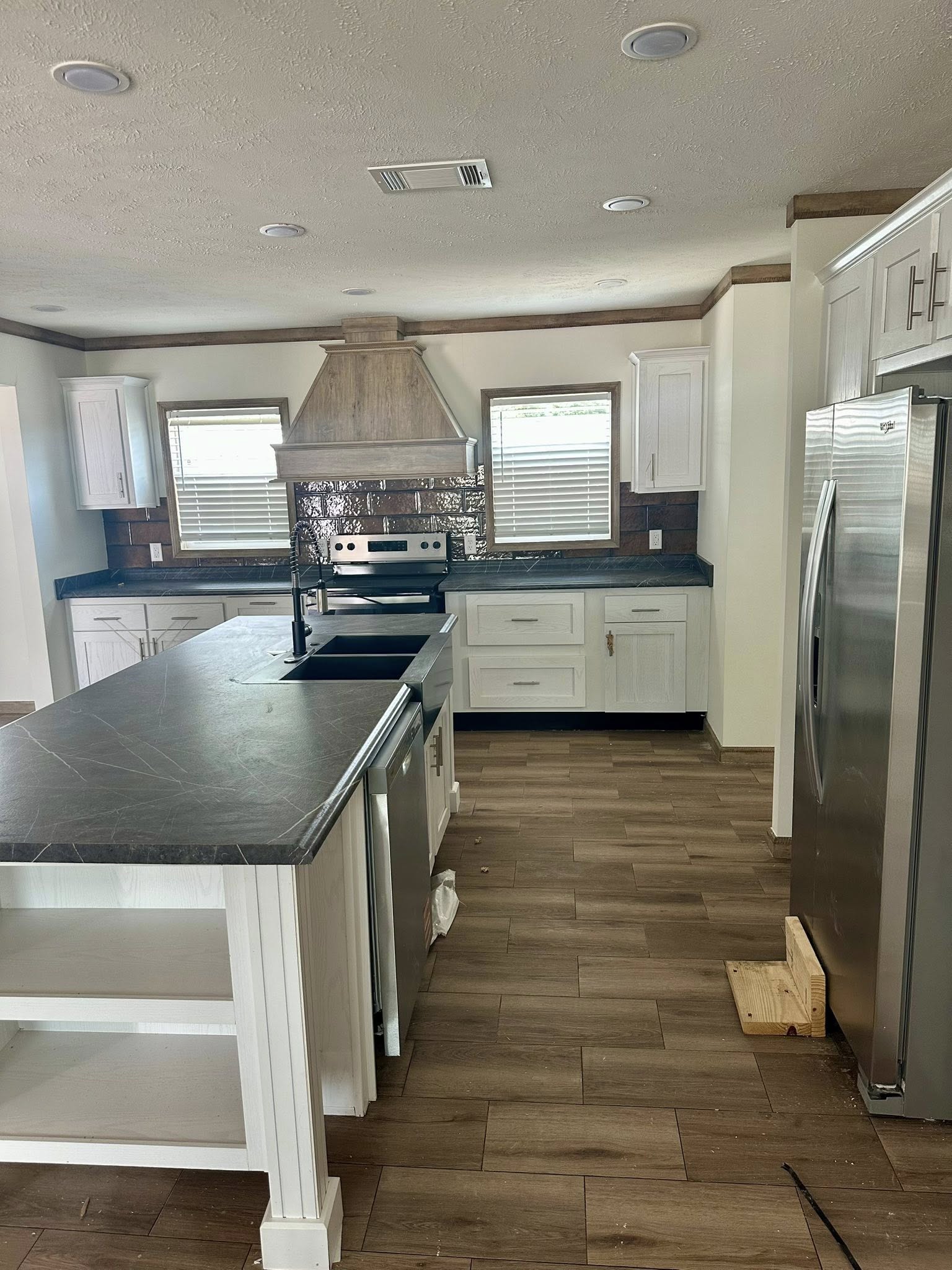 Modern kitchen with stainless steel appliances, white cabinets, and a dark countertop island. Two windows illuminate the space, creating a welcoming atmosphere.