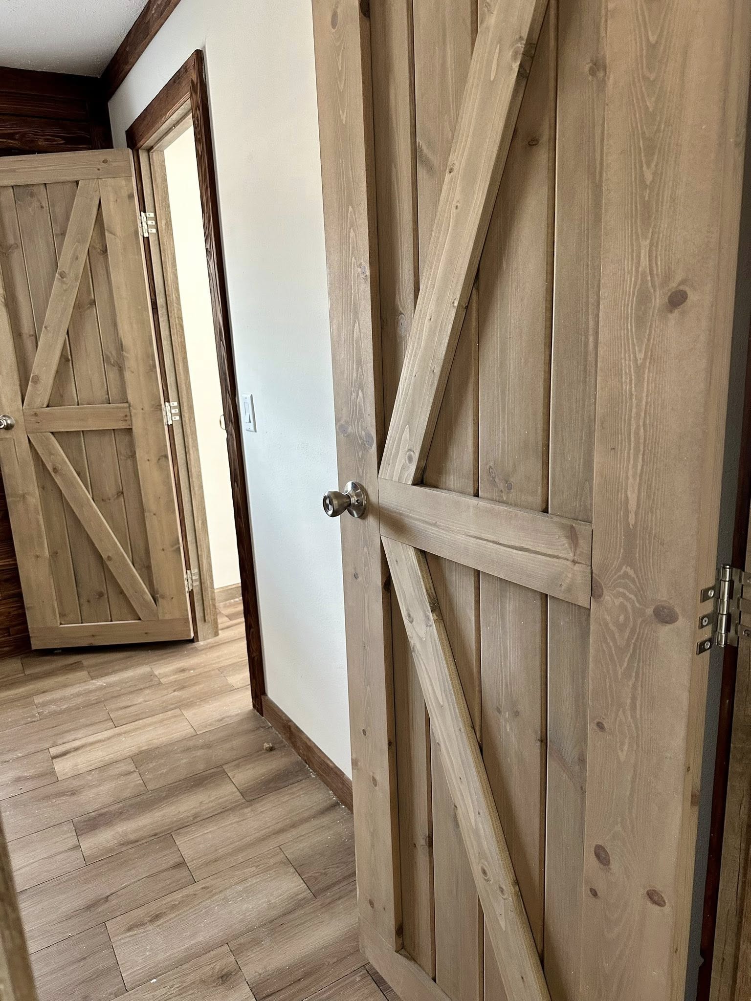 Wooden interior doors with a rustic barn-style design; one slightly ajar. Light wood flooring and white walls provide a cozy, country feel.