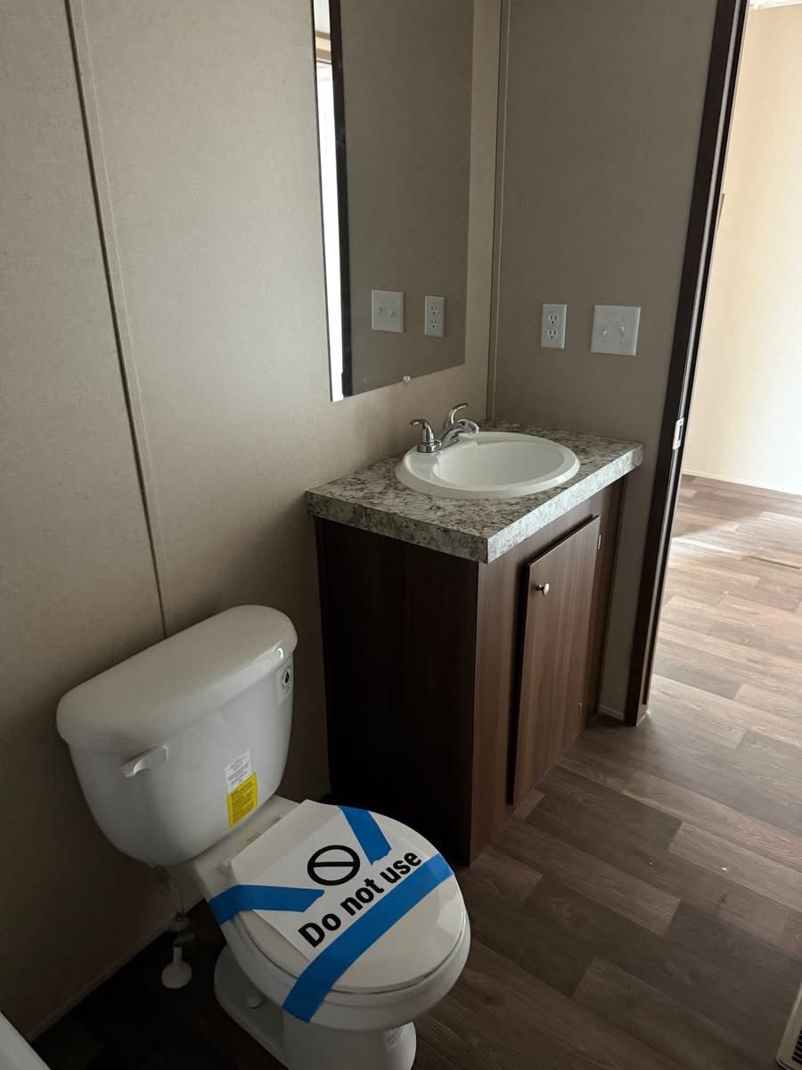 Bathroom with a white toilet marked "Do not use" with blue tape. Wooden cabinet with sink and mirror above. Neutral tones, clean and minimalistic.