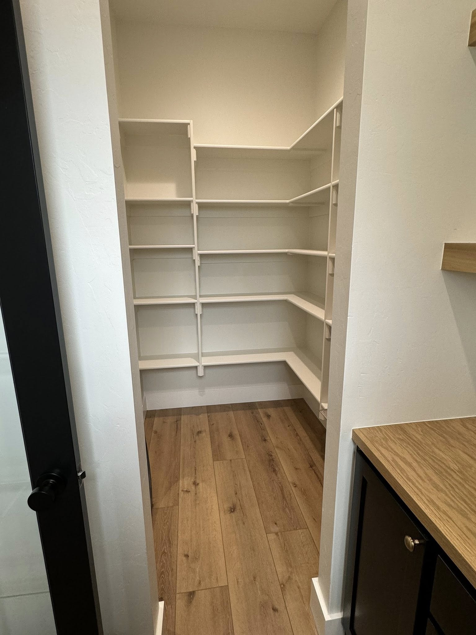 A small, empty walk-in pantry with white shelves on three walls and a wooden floor. The bright space feels clean and organized, ready for use.