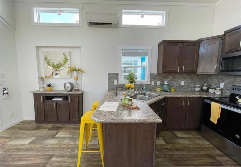 Compact kitchen with dark wood cabinets, gray countertops, and a tiled backsplash. Yellow stools at the counter add a pop of color. Bright accents like flowers and lemons enhance the inviting and cheerful atmosphere.