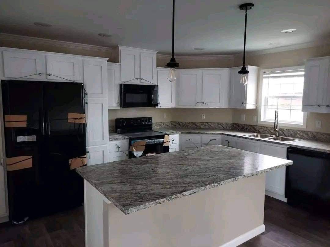 Modern kitchen with white cabinets, granite countertops, and dark appliances. Features a central island, pendant lights, and a window for natural light.