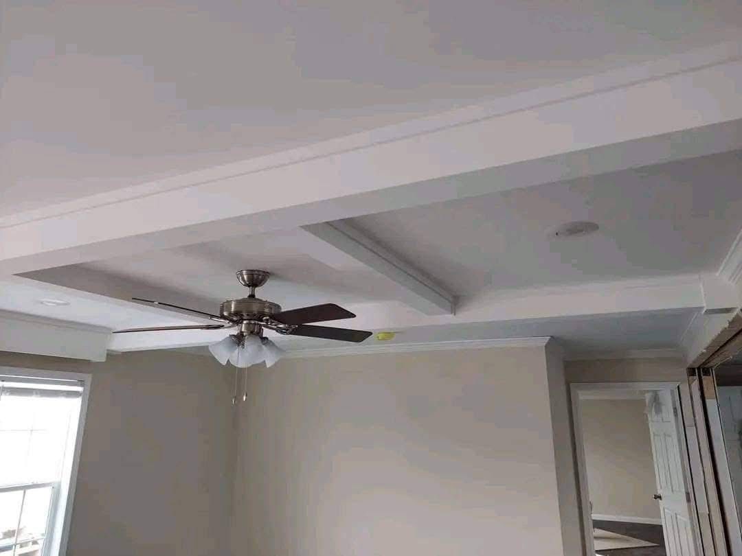 Ceiling with modern design features a central fan with wooden blades and frosted glass shades. Soft beige walls and an open doorway create an airy feel.