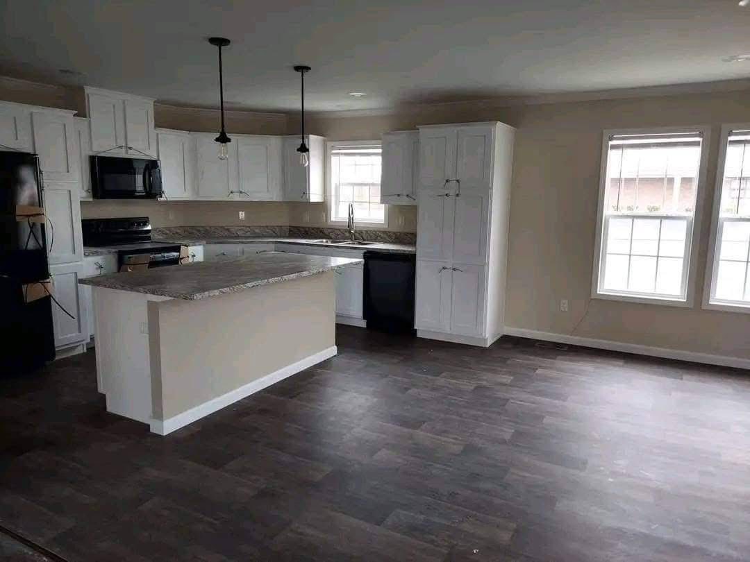 Spacious kitchen with white cabinets, granite countertops, and dark wood flooring. Features an island, pendant lights, and large windows.